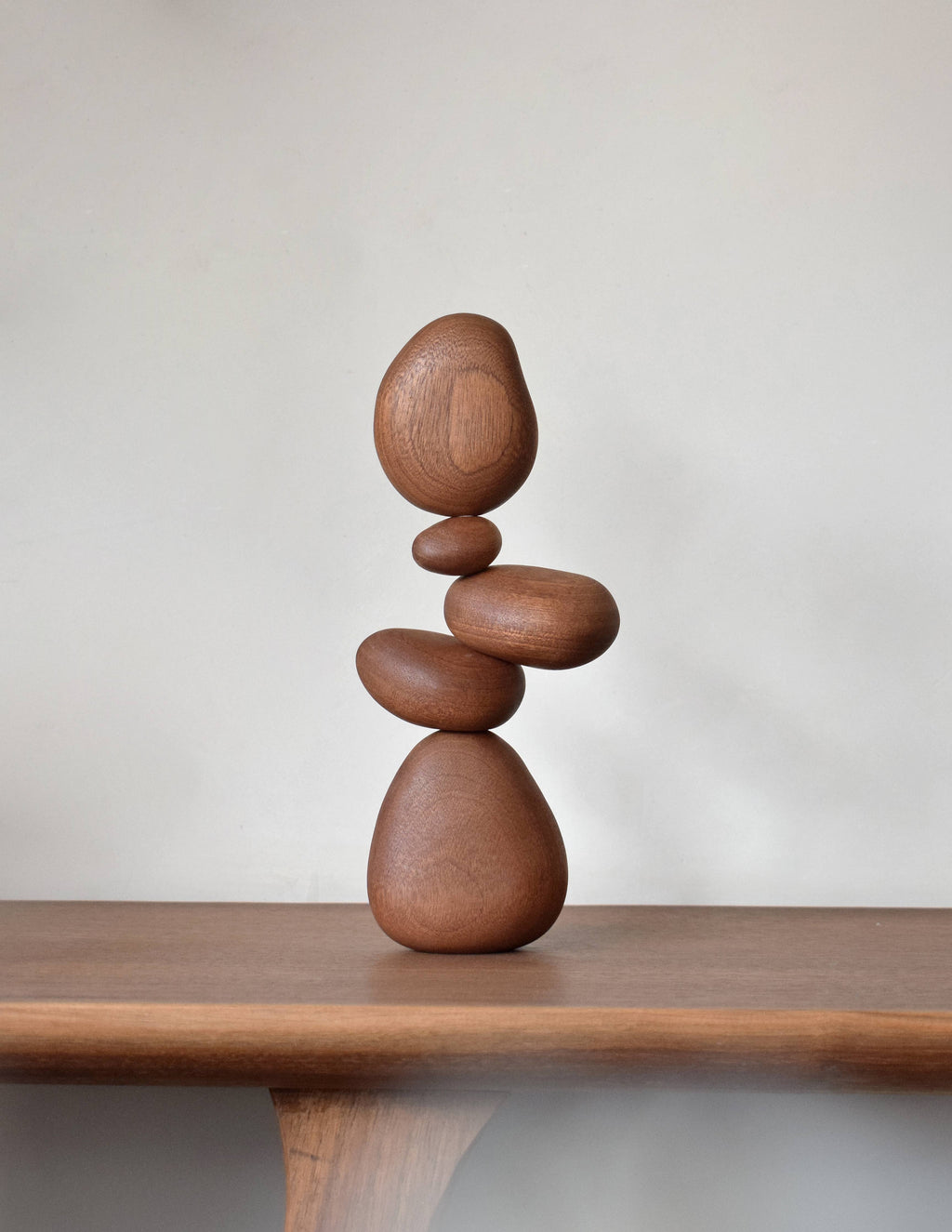 Five sapele wood balance stones stacked into a leaning cairn on a walnut shelf