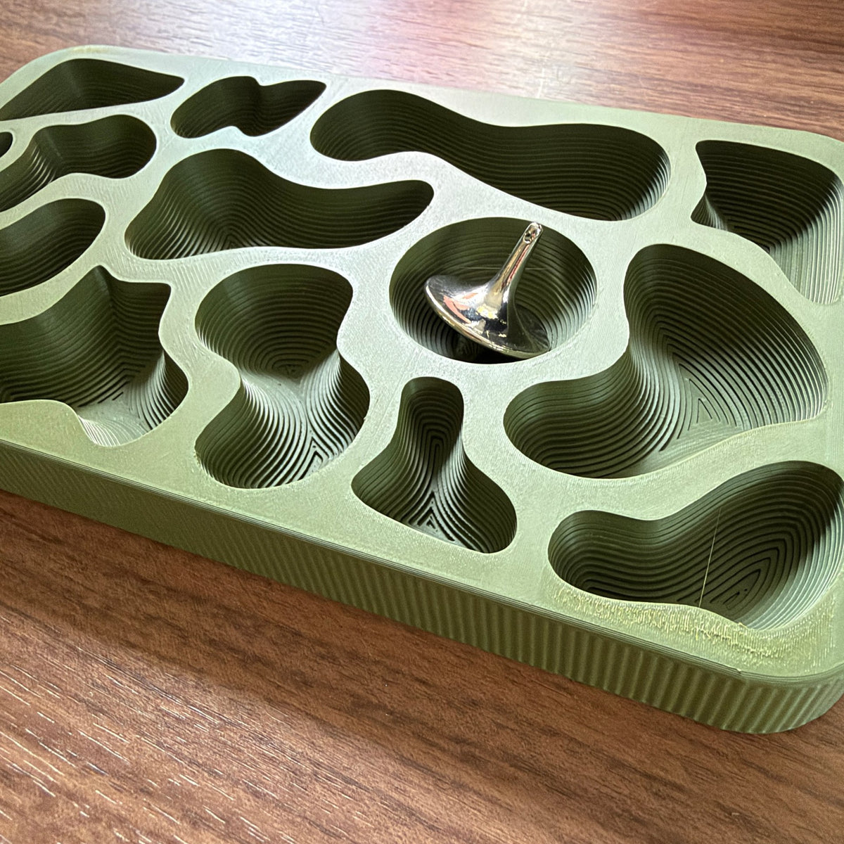 Topography Tray on a walnut desk with a steel spinning top in its round well
