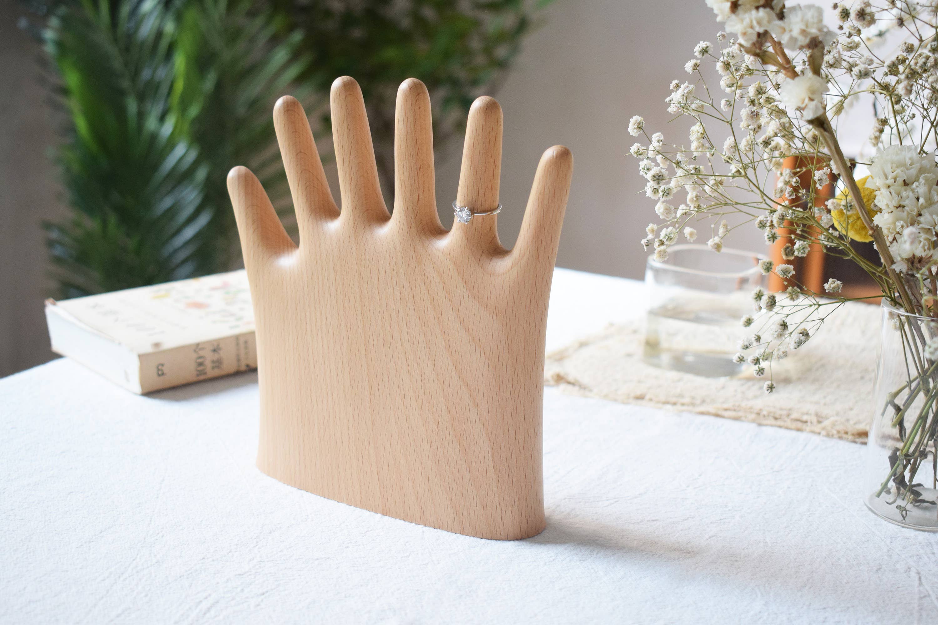 The palm stand on a linen tablecloth beside dried flowers and a book, a ring on one finger
