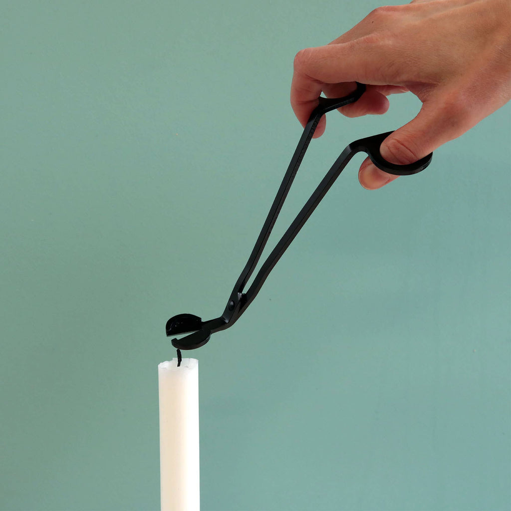 A hand using the wick trimmer to cut the wick of a lit white taper