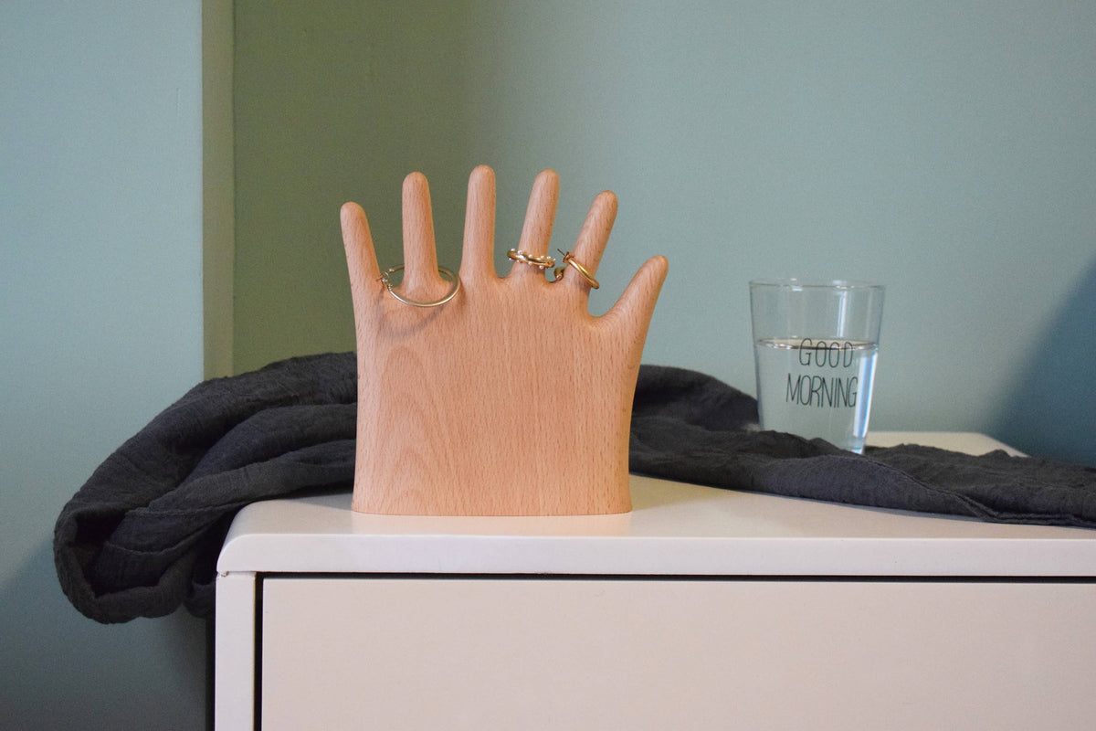 The OK hand on a white sideboard against a sage green wall, rings on two fingers
