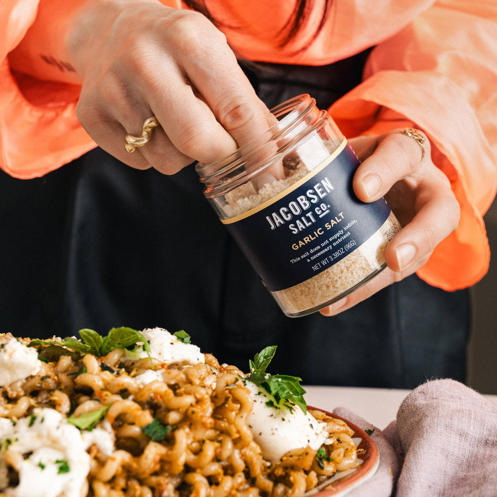 Hands holding a jar of Jacobsen Garlic Salt above a plate of pasta