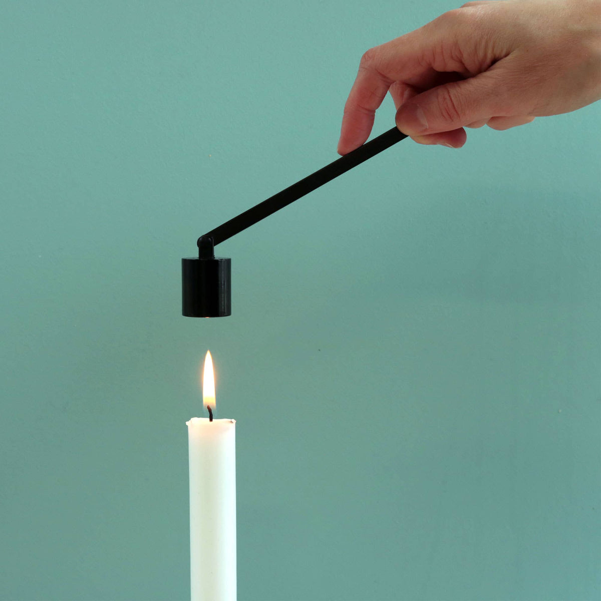 The bell snuffer lowered over a lit taper, about to put the flame out