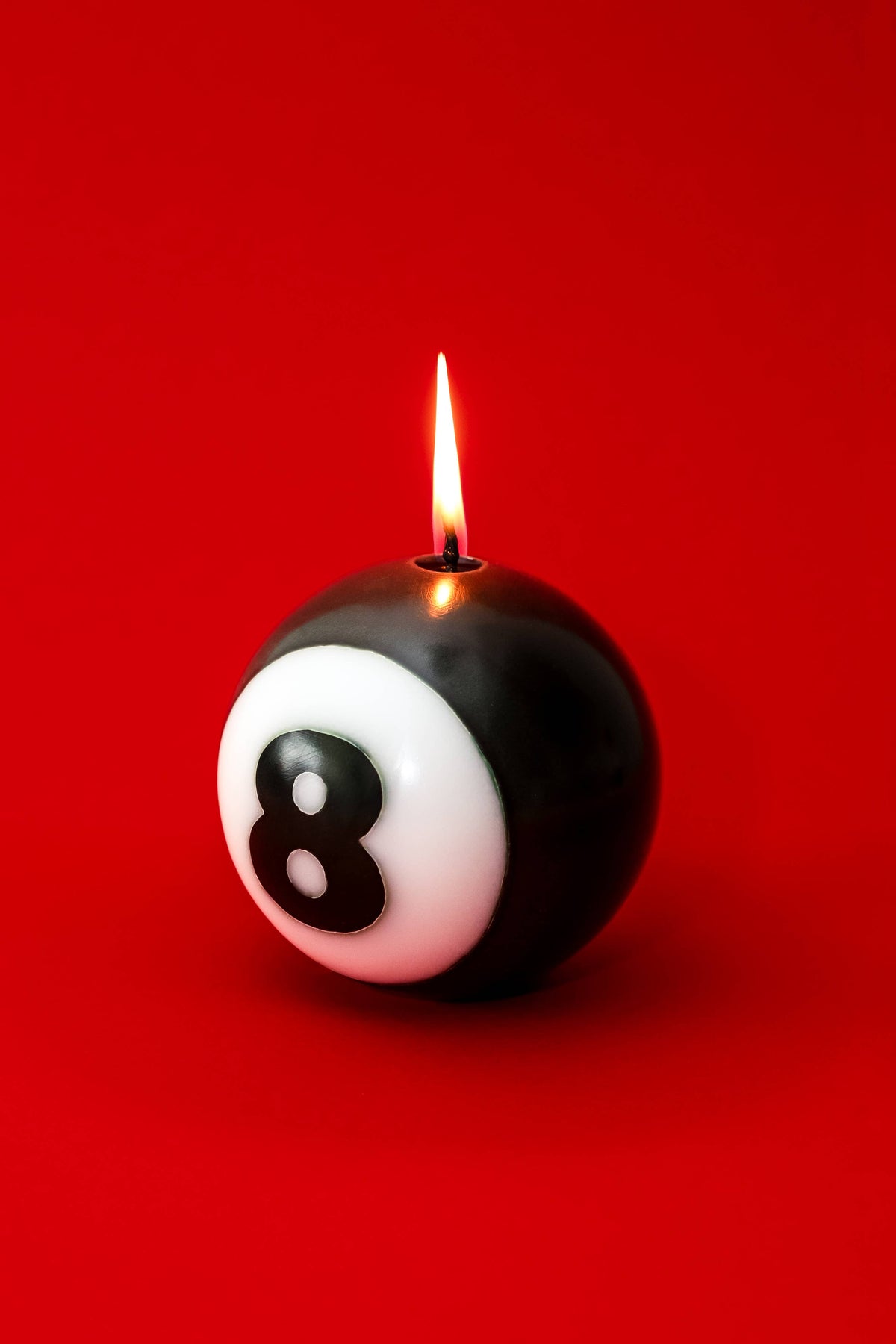 Classic 8-Ball candle burning against a deep red ground