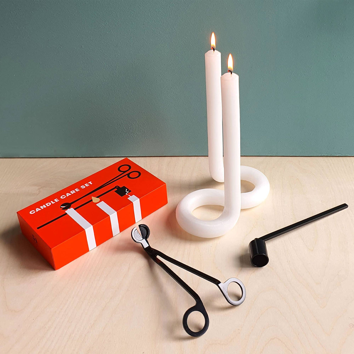 The red Candle Care Set box beside two lit tapers, with the snuffer and trimmer in front