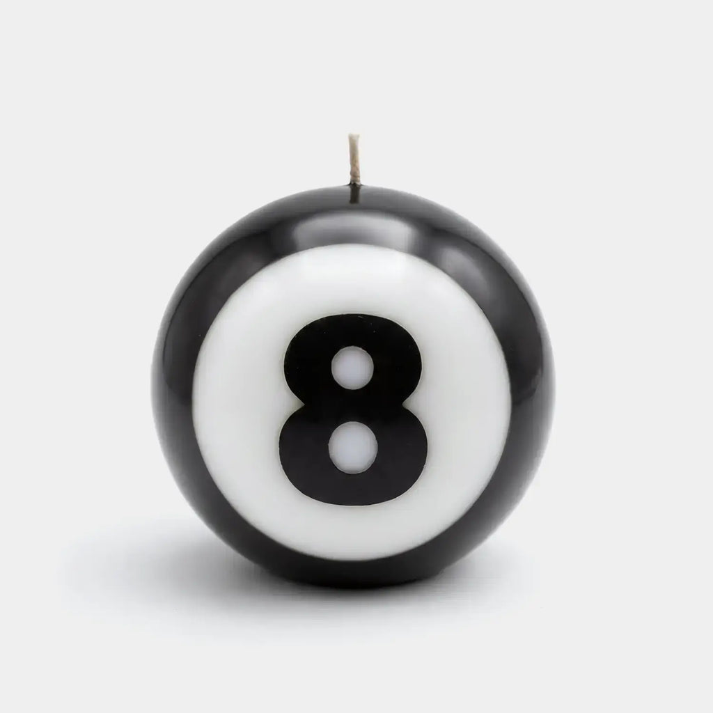 Classic 8-Ball candle burning on a white ground with a soft shadow beneath it