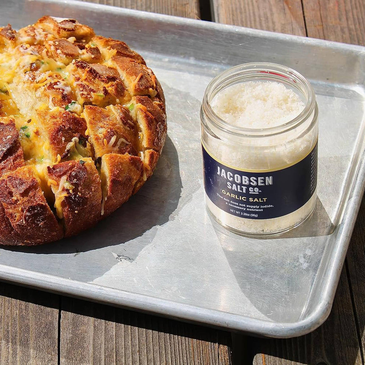 Open jar of Jacobsen Garlic Salt on a baking sheet next to a golden pull apart bread