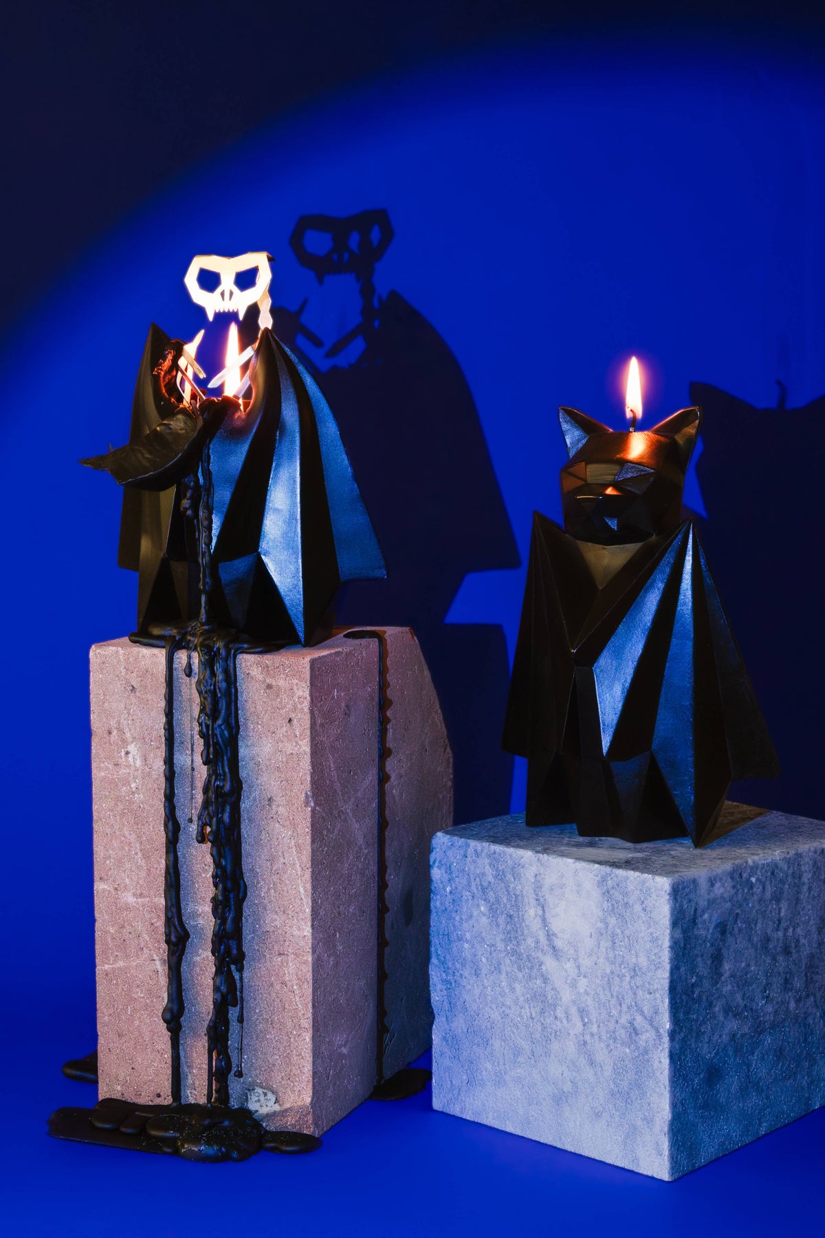 Two Blaka bat candles burning on stone plinths against a deep blue ground, skulls lit from within