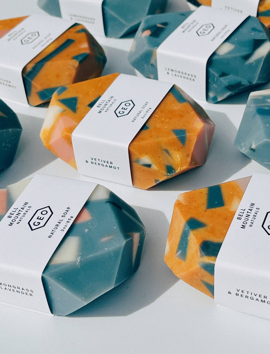 Faceted terrazzo gem soaps in teal and orange with speckled chips, each wrapped in a white Bell Mountain Naturals band