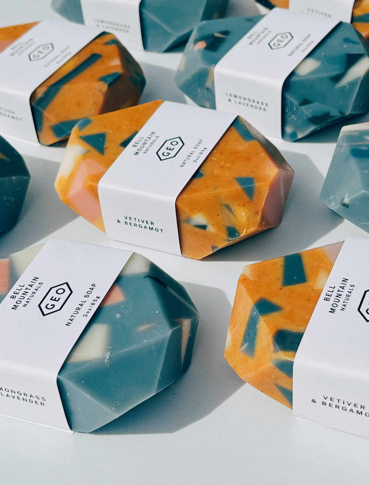 Faceted terrazzo gem soaps in teal and orange with speckled chips, each wrapped in a white Bell Mountain Naturals band