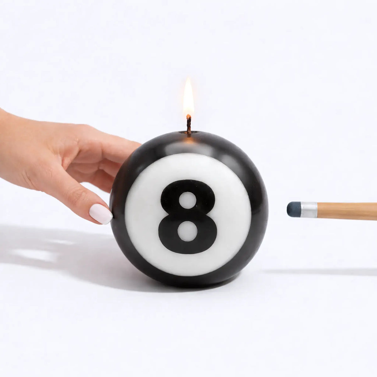 A hand lighting the Classic 8-Ball candle with a long match