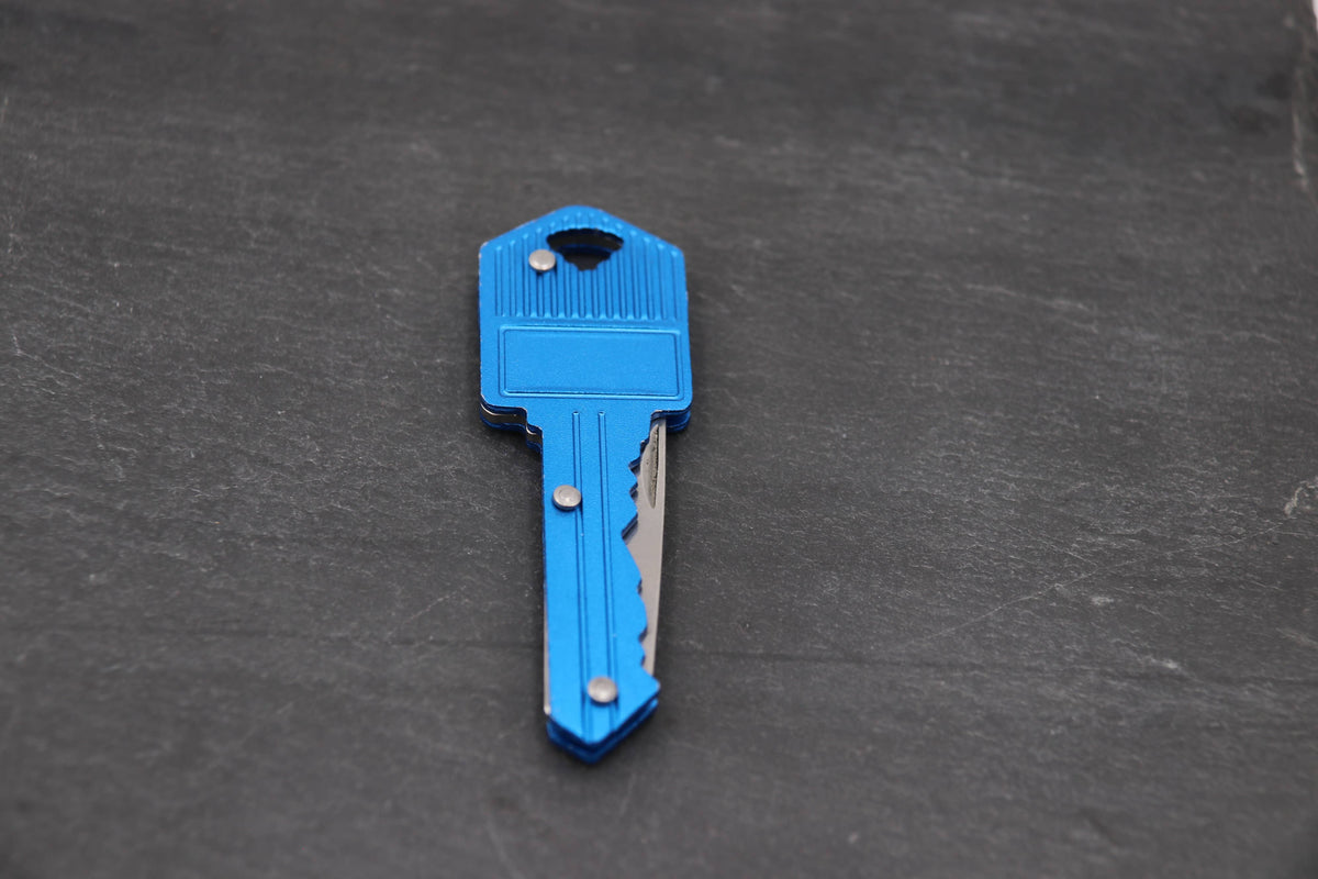 Bright blue key shaped folding knife on dark slate, the small blade tucked along the key