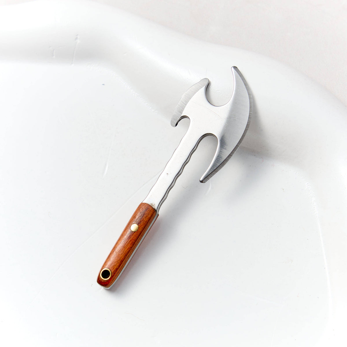 Mini battle axe keychain knife with a polished silver double edged head and a wooden handle, lying on white stone