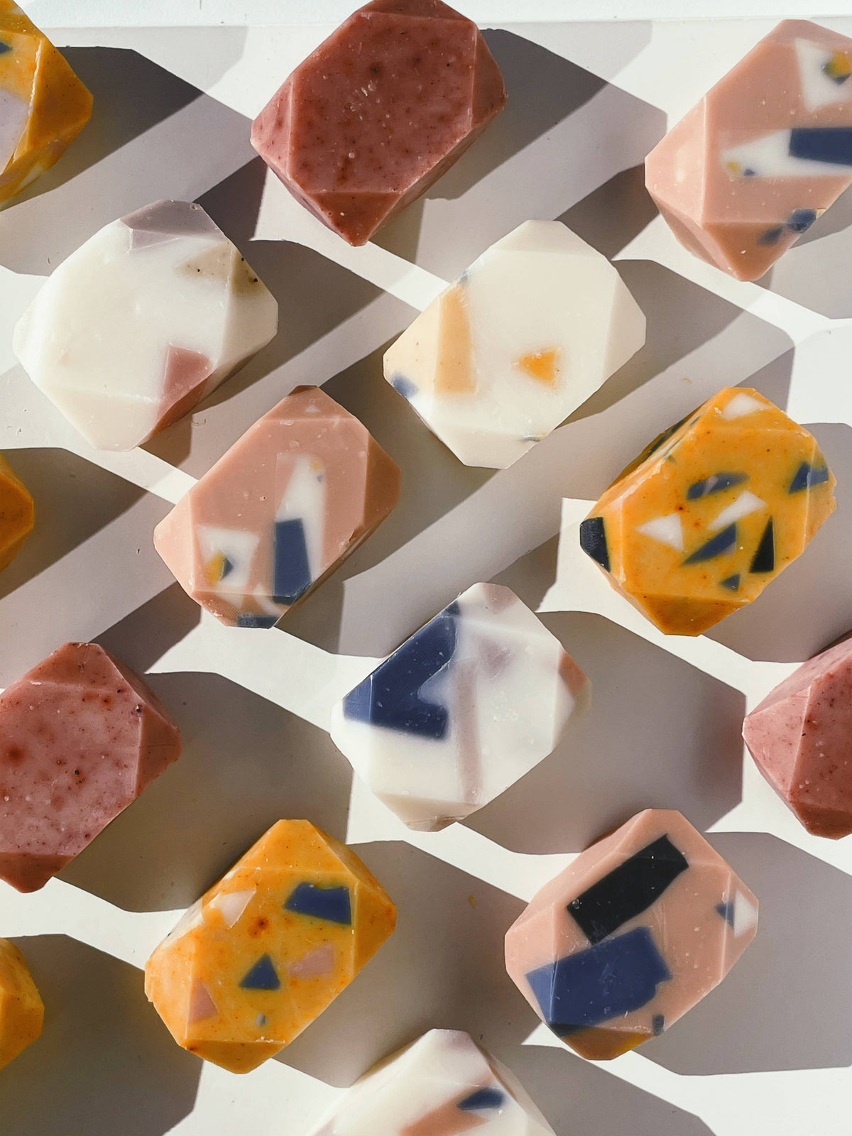 Mini terrazzo gem soaps laid out in rows, pale pink, cream and amber with navy and orange chips set through them