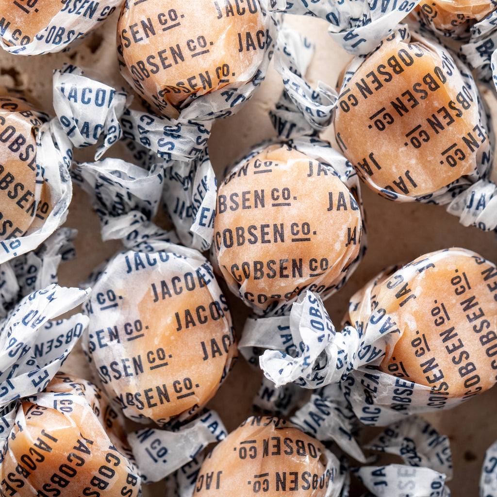 Pile of Jacobsen salted caramels twisted in white paper wrappers printed with the Jacobsen Co. name in navy