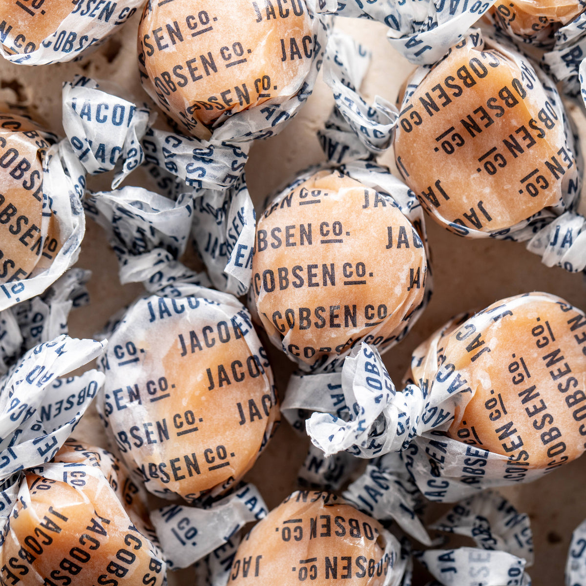 Pile of Jacobsen salted caramels twisted in white paper wrappers printed with the Jacobsen Co. name in navy