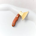 Mini hatchet keychain knife with a gold steel head and a reddish wooden handle, lying on white stone