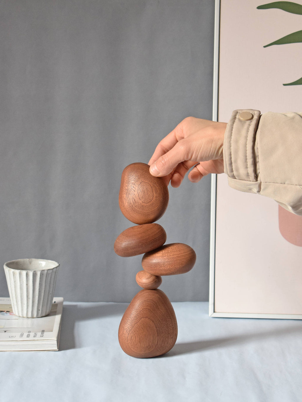 A hand placing the top stone on a balanced stack, on a desk beside a coffee cup