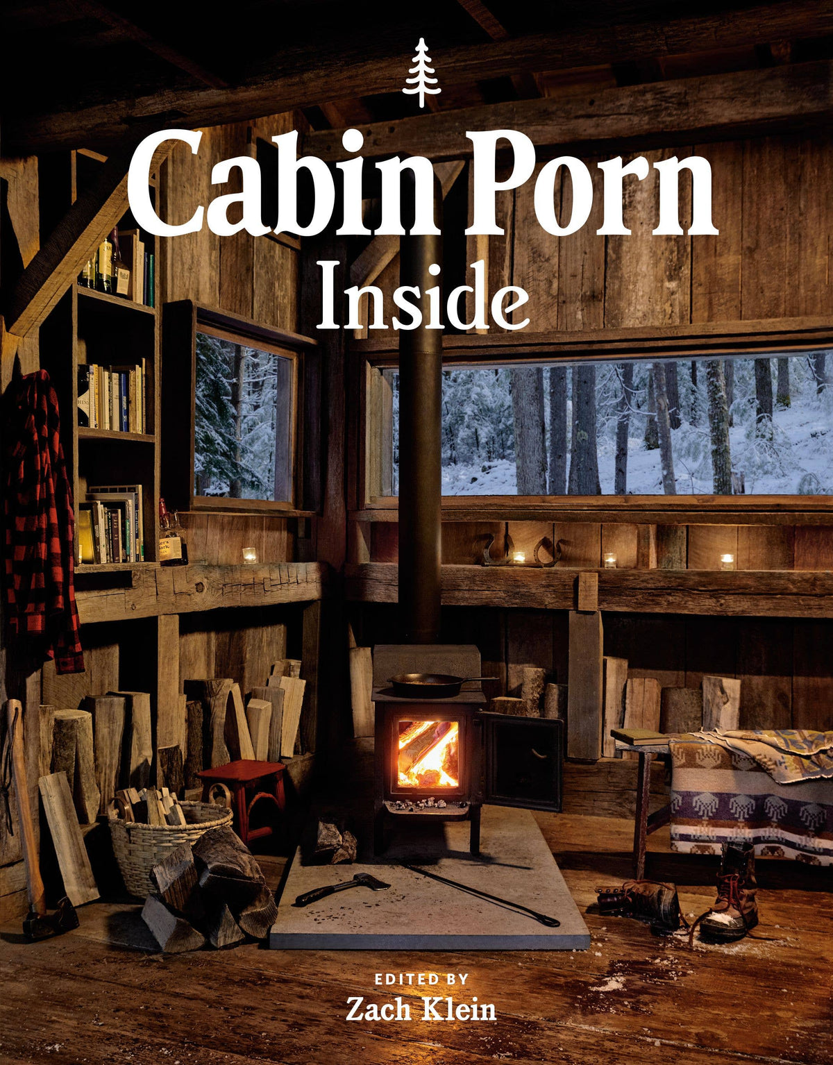Cabin Porn: Inside cover: a dim wooden cabin interior with shelves, a wood stove glowing and a snowy view through tall windows
