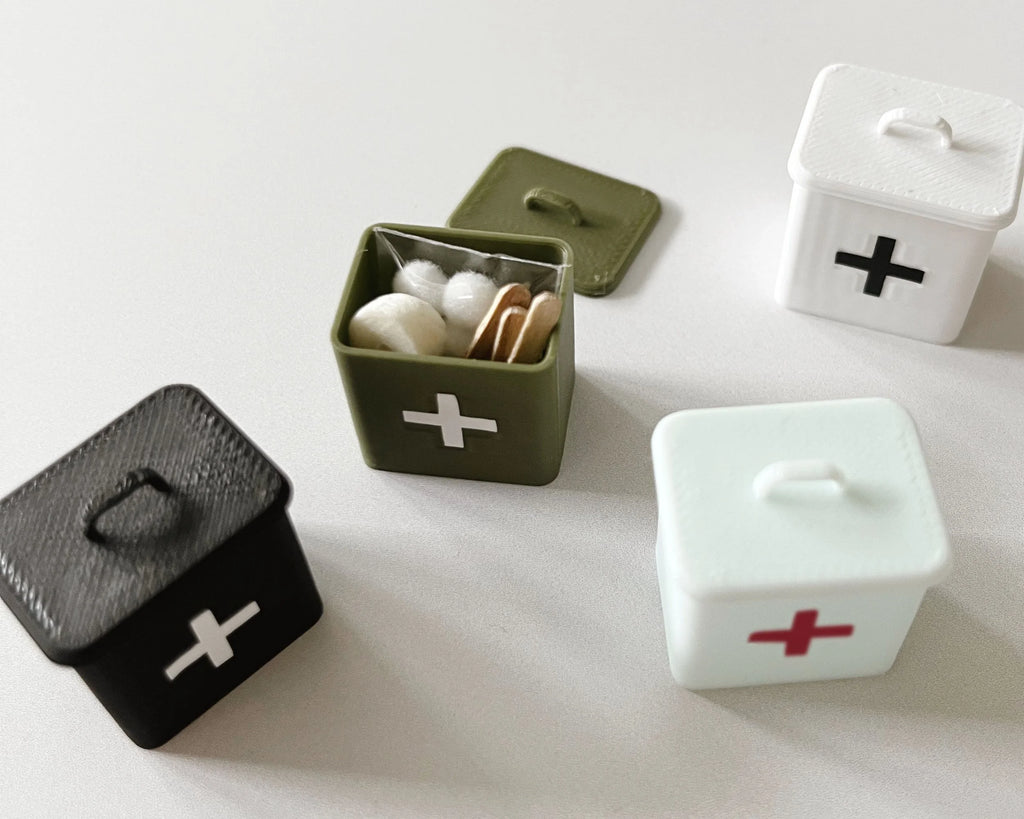 The olive miniature first aid box open and packed with cotton and supplies, shown with Miniette boxes in other colors