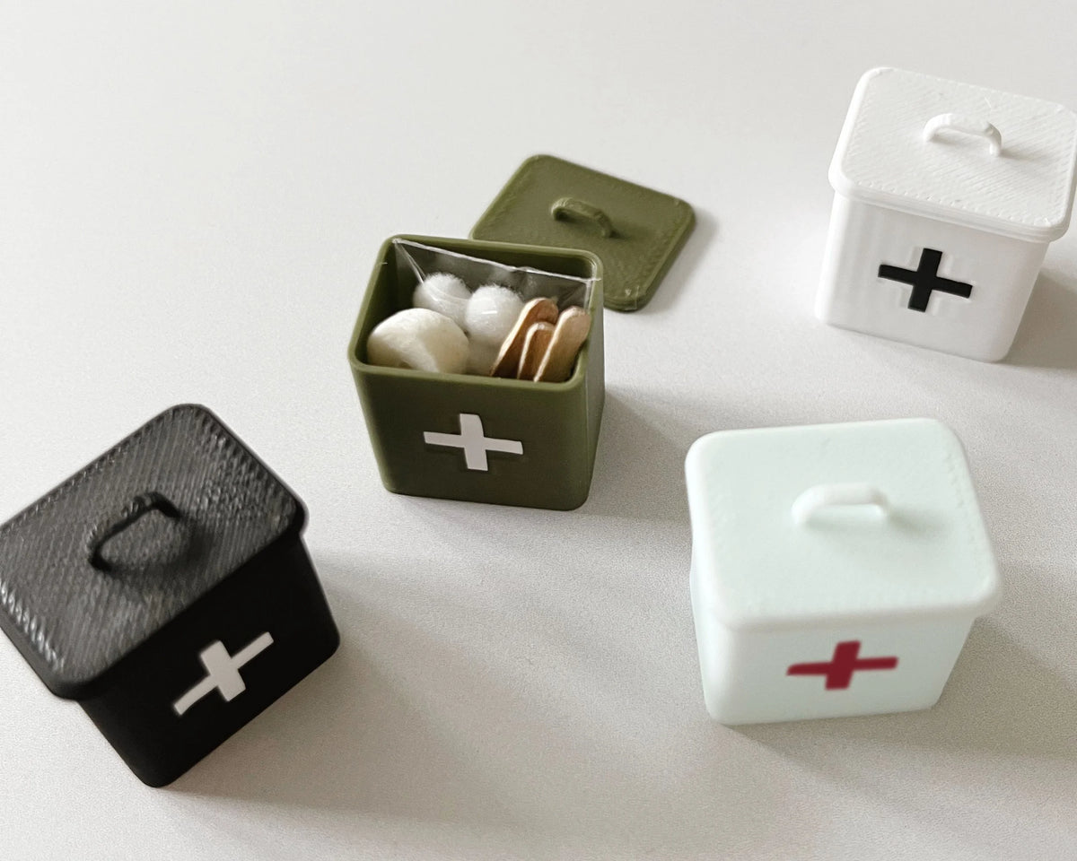 The olive miniature first aid box open and packed with cotton and supplies, shown with Miniette boxes in other colors