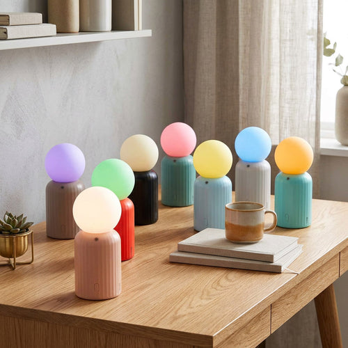 Nine mini wireless lamps grouped on a wooden desk, ribbed pastel bases with glowing globe bulbs in purple, green, amber, pink, yellow, blue and orange