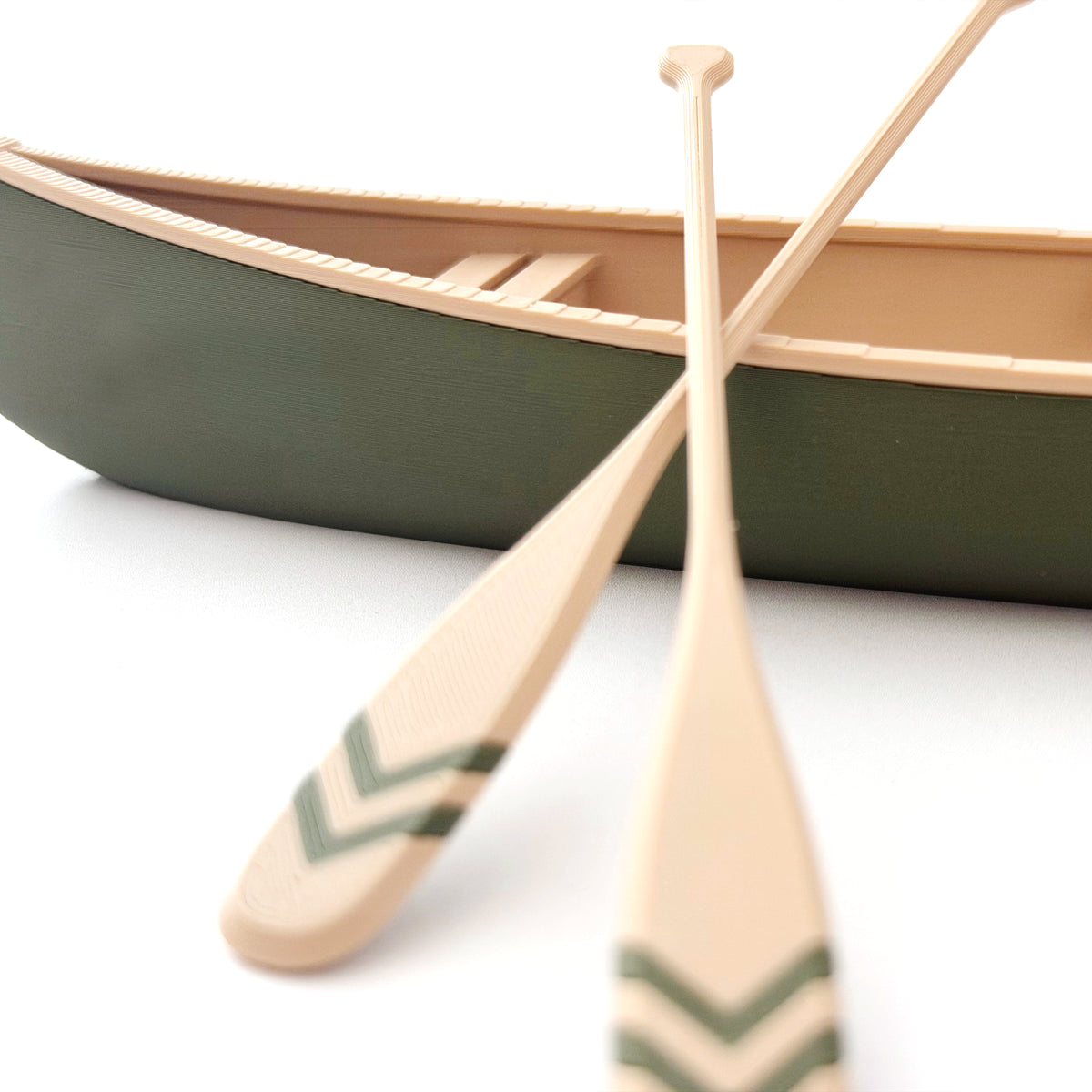 Close up of the two miniature canoe oars, natural wood color with green chevrons painted on each blade, resting against the green hull