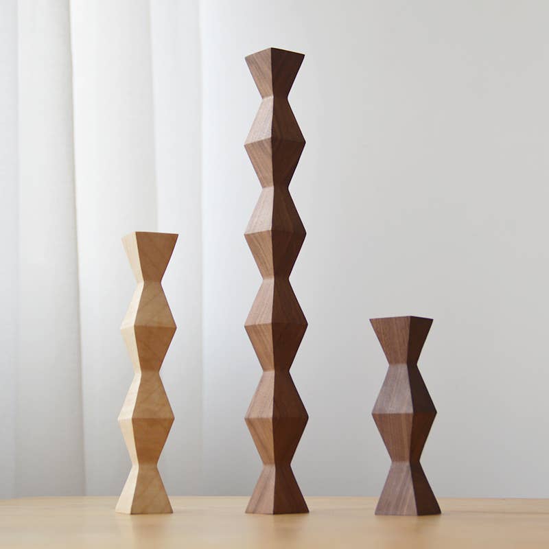 Three Endless Column wood sculptures in graduated sizes, faceted modules stacked into slender towers in pale beech and dark walnut, on a light wood table