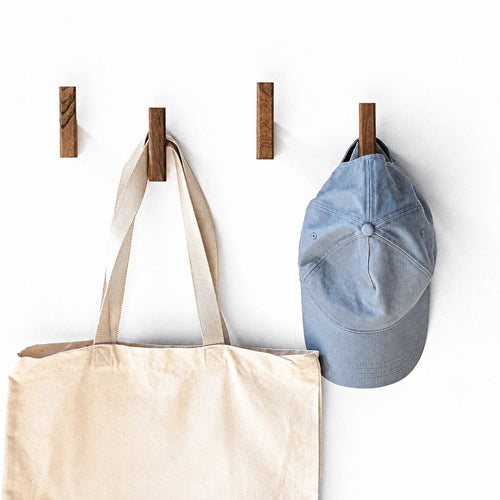 Solid wood wall coat hooks in walnut mounted in a row, holding a canvas tote and a denim cap