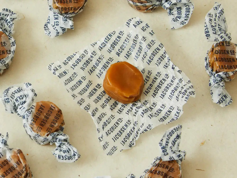One unwrapped Jacobsen caramel resting on its printed paper wrapper, with wrapped caramels around it