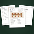 Three pages of The Dinner Party hosting kit fanned on moss green, the first page showing a wooden table from above set with six plates and three candles