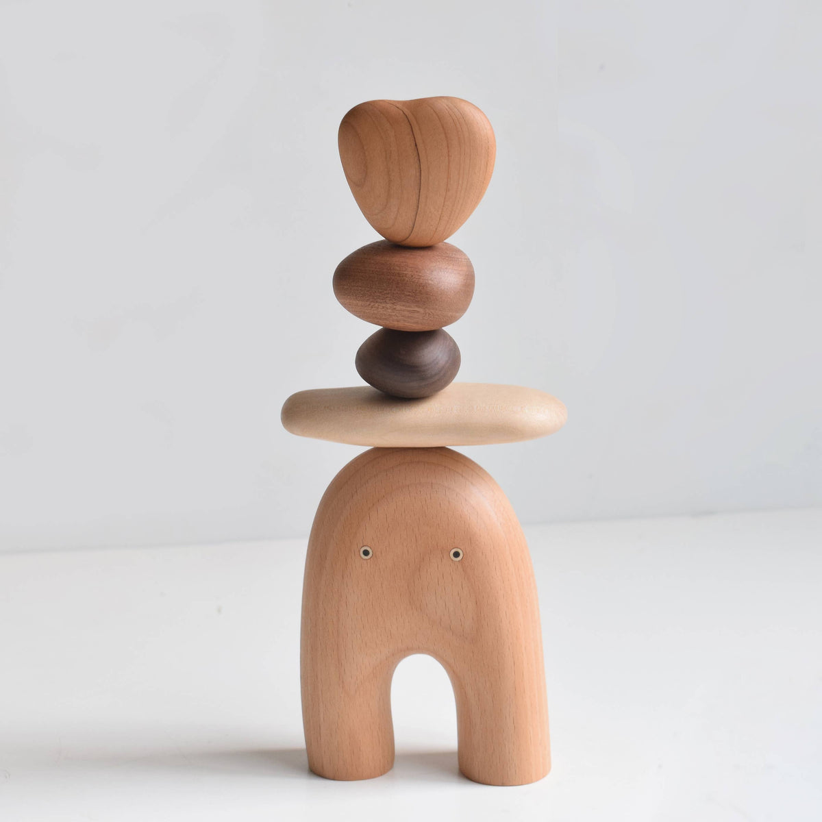 Balance Elf wood sculpture, a rounded beech body with arched legs and two small eyes, topped with a stack of smooth walnut, cherry and maple shapes