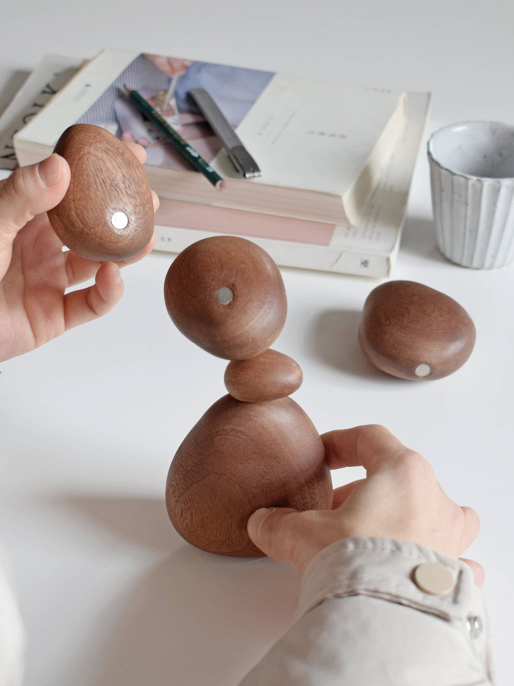 Hands rebuilding the stone stack on a desk, with the smallest stone on top