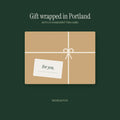 A kraft paper parcel tied with cream twine and a handwritten For you card, on a deep green ground