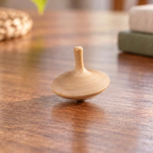 Hand carved oak spinning top standing on its point on a wooden table