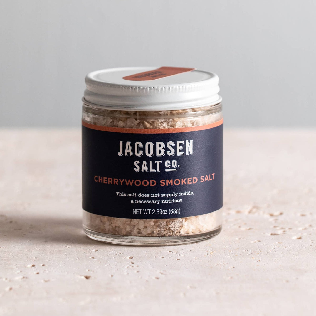 Jar of Jacobsen Cherrywood Smoked Salt, 2.39 oz, with a navy label and white lid on a pale stone table