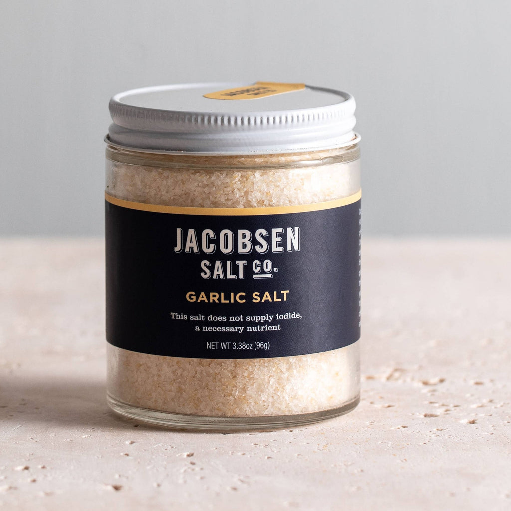 Jar of Jacobsen Garlic Salt, 3.38 oz, navy label with a gold stripe, on a pale stone table