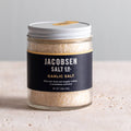 Jar of Jacobsen Garlic Salt, 3.38 oz, navy label with a gold stripe, on a pale stone table