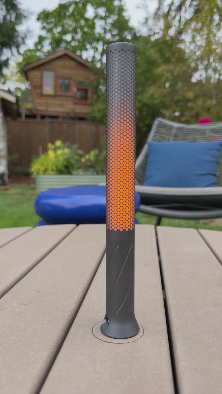 Flameless candle light standing on a wooden deck, its amber flicker mode rising and falling through the perforated metal
