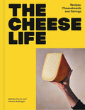 The Cheese Life hardcover, bright yellow cover with the title in heavy black type and a hand holding up a wedge of cheese