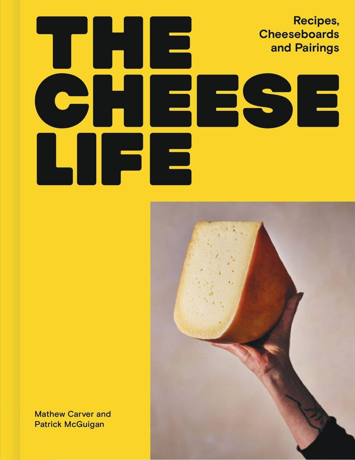 The Cheese Life hardcover, bright yellow cover with the title in heavy black type and a hand holding up a wedge of cheese