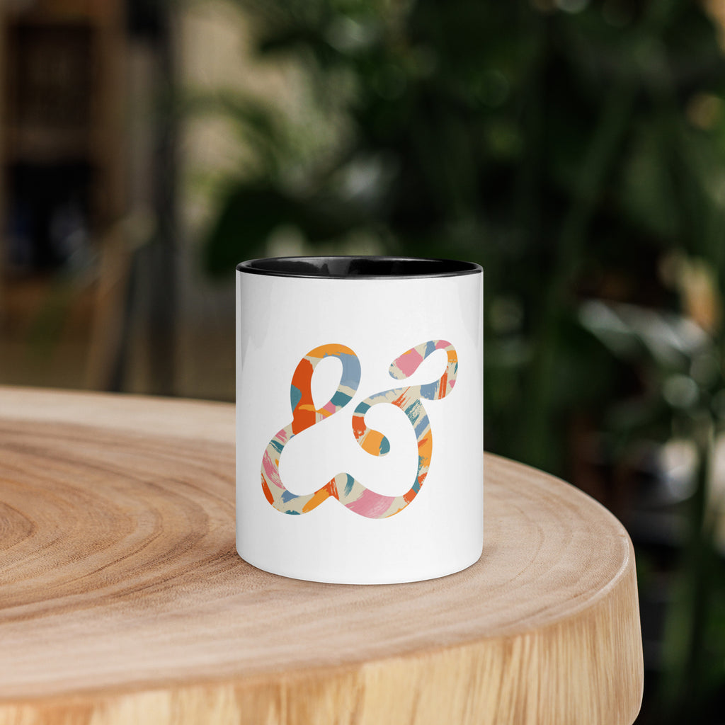 White ceramic mug with a black inside and handle, printed with the colorful painted Moss and Fog ampersand
