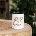 White ceramic mug with a black inside and handle, printed with the colorful painted Moss and Fog ampersand