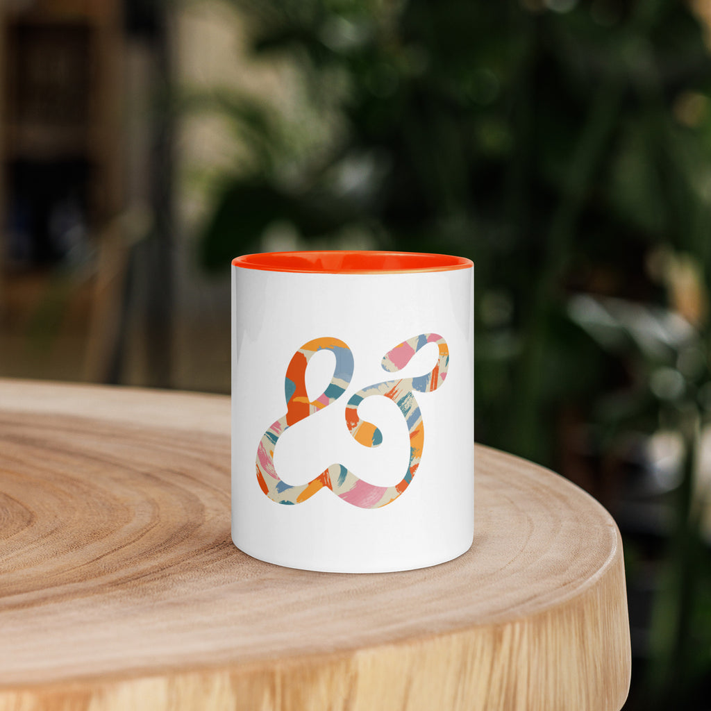 White ceramic mug with an orange inside and handle, printed with the painted Moss and Fog ampersand